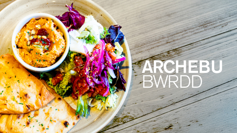 Plat o fwyd lliwgar gyda bara ar yr ochr a geiriau Archebu Bwrdd